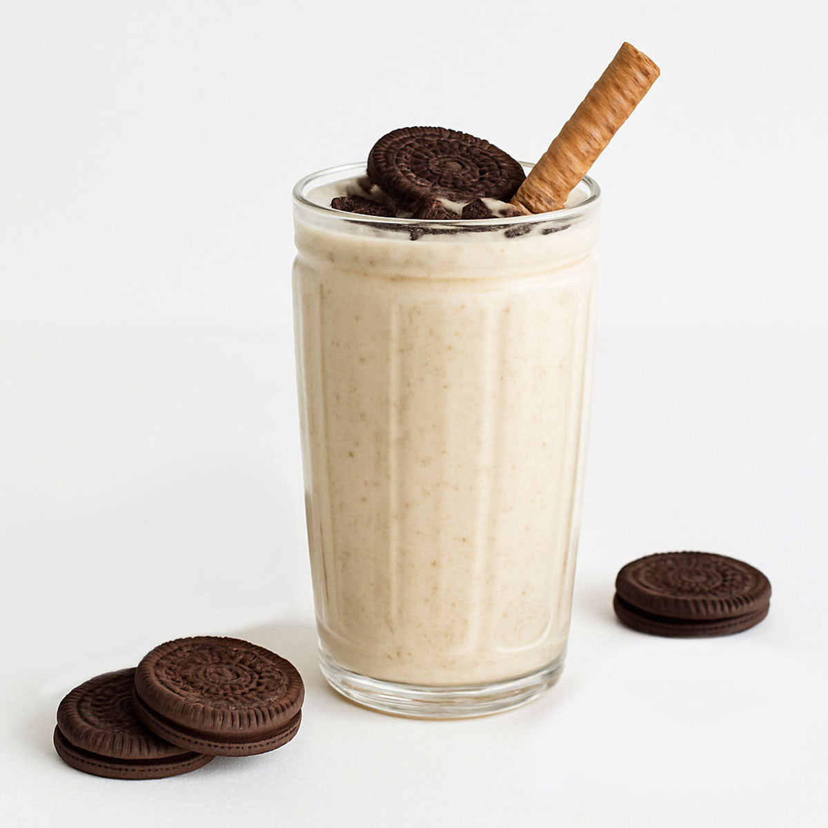 Glass of milkshake with Oreo cookies and a cinnamon stick on a white background