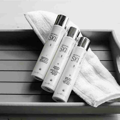 Three SKIN skincare bottles on a wooden surface with a towel.