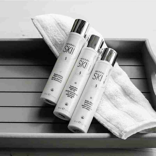 Three SKIN skincare bottles on a wooden surface with a towel.